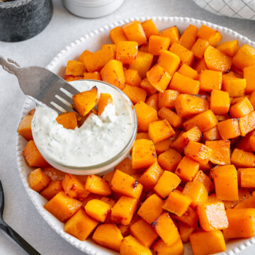 Air fryer butternut squash cubes and a small bowl of tzatziki in a white bowl with a white background.