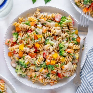 Tahini pasta salad on a white plate served with a silver fork with a white background.