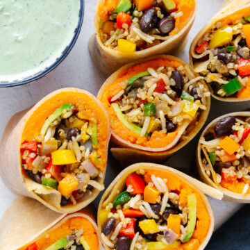Vegan breakfast burritos on a white background next to a bowl of cilantro sauce.