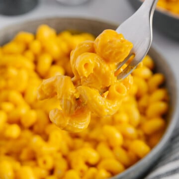 A fork holding a bite of carrot sauce pasta over the bowl of pasta.