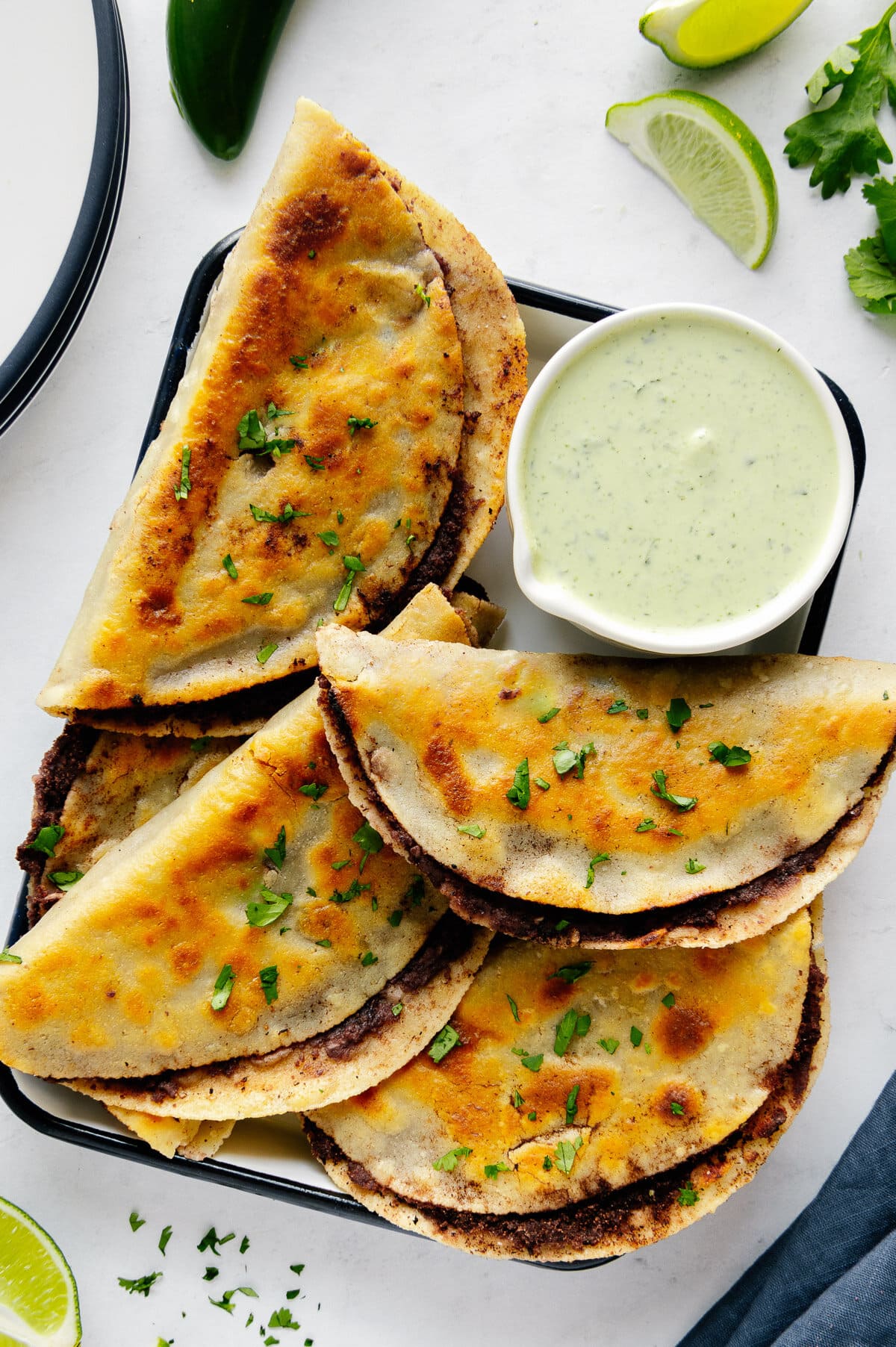 Fried black bean tacos piled on a rectangular white plate served with a small bowl of cilantro sauce.