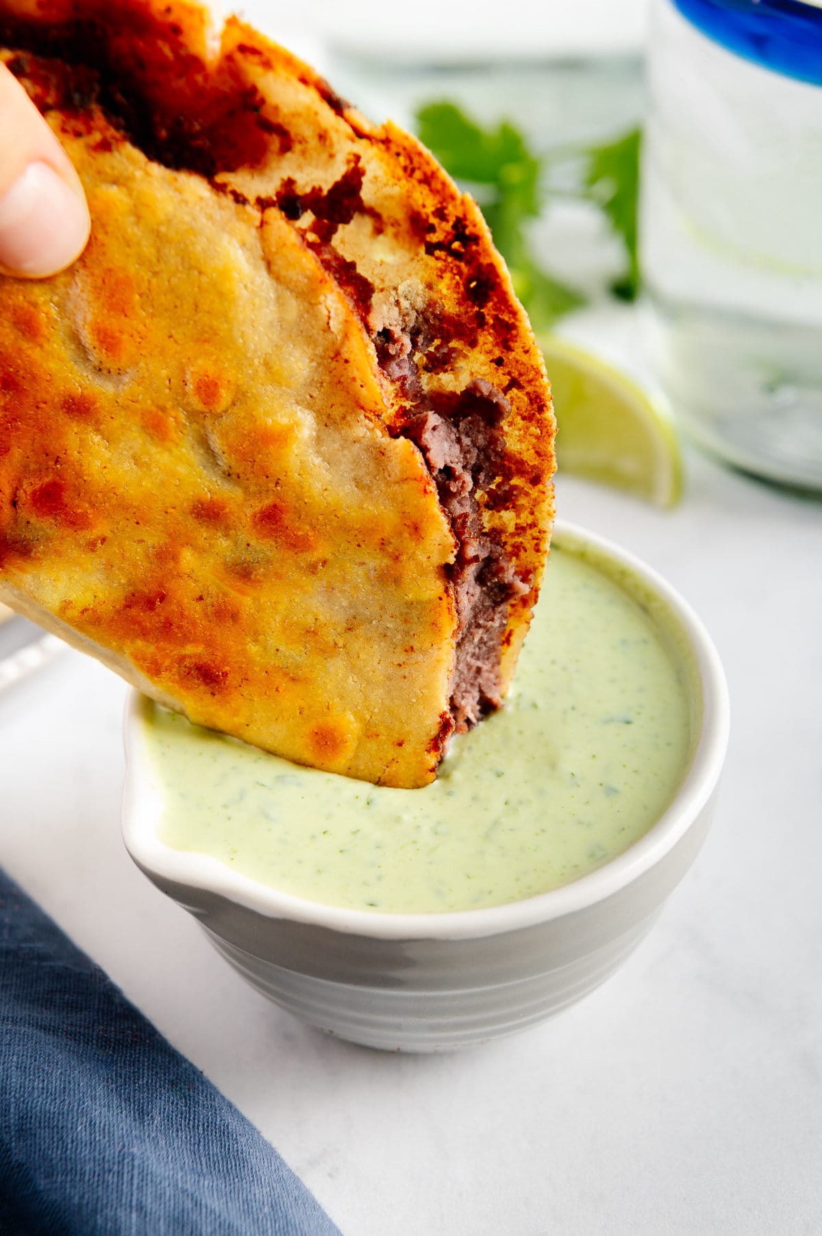 A crispy fried black bean taco being dipped in creamy cilantro sauce.