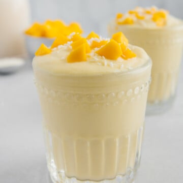 Mango pineapple smoothie garnished with mango chunks with a light gray background.