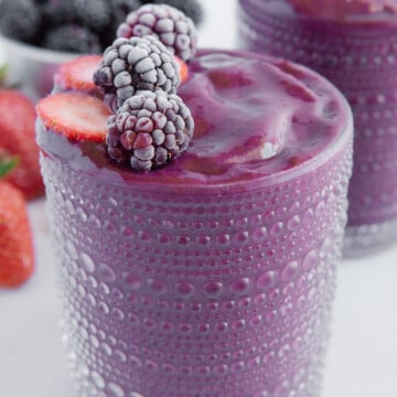 Strawberry blackberry smoothie in a glass cup garnished with strawberries and blueberries.
