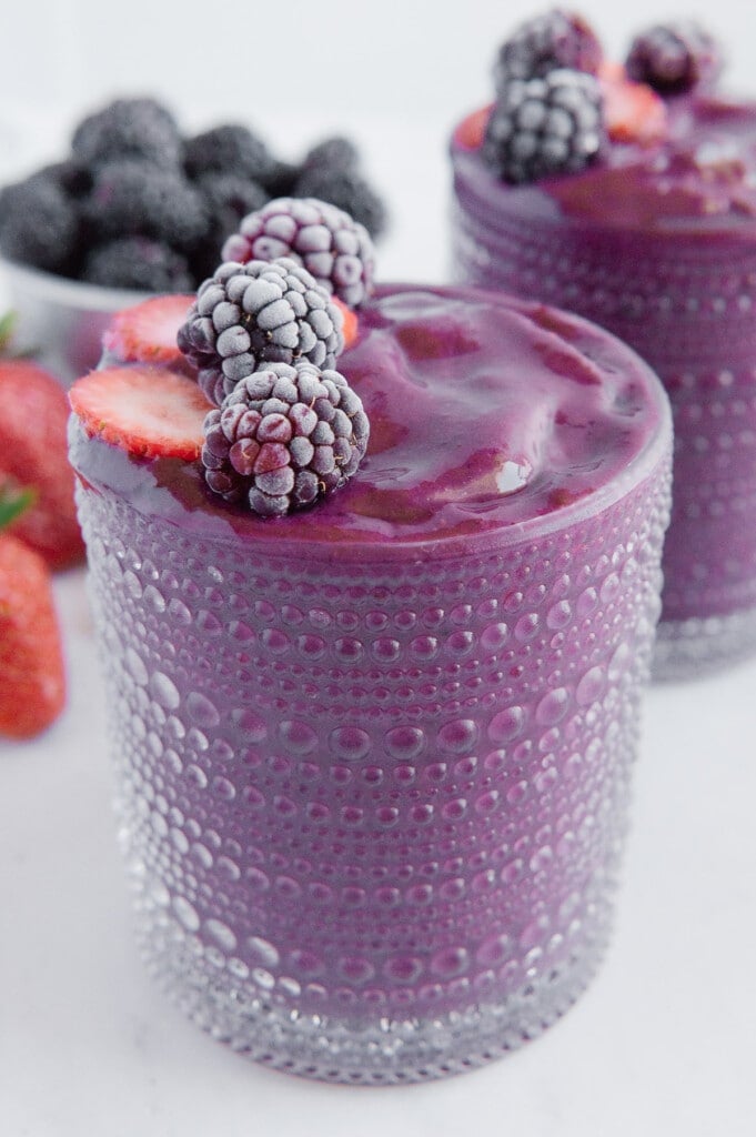 Strawberry blackberry smoothie in a glass cup garnished with strawberries and blueberries.