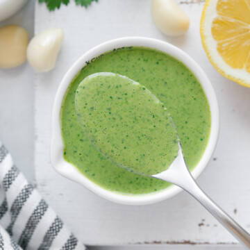 A spoonful of lemon herb tahini sauce over the bowl of sauce with a white background.