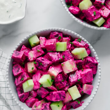 Beet cucumber salad in a white bowl with garlic dill dressing with a marble white background.