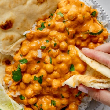A hand using folded naan to scoop up vegan butter chickpeas.