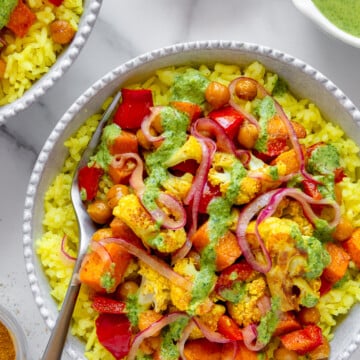 Roasted curry veggie bowl over turmeric rice topped with a jalapeño herbed tahini dressing in a white bowl.