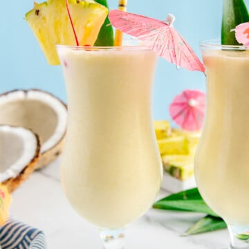Pina colada mocktail garnished with a drink umbrella, straw and pineapple wedge with a sky blue background.