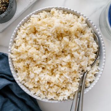 Quinoa rice in a white bowl next to a blue cloth with a white marble background.