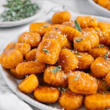 Sweet potato gnocchi topped with fresh herbs and vegan parmesan with a white background.
