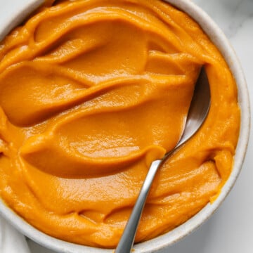 Sweet potato puree in a white bowl with a spoon and white marble background.