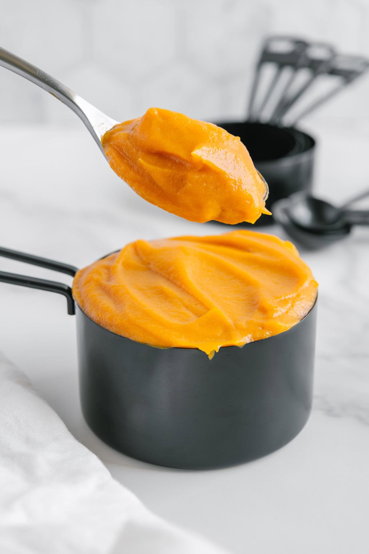 Sweet potato puree in a black measuring cup with a white marble background.