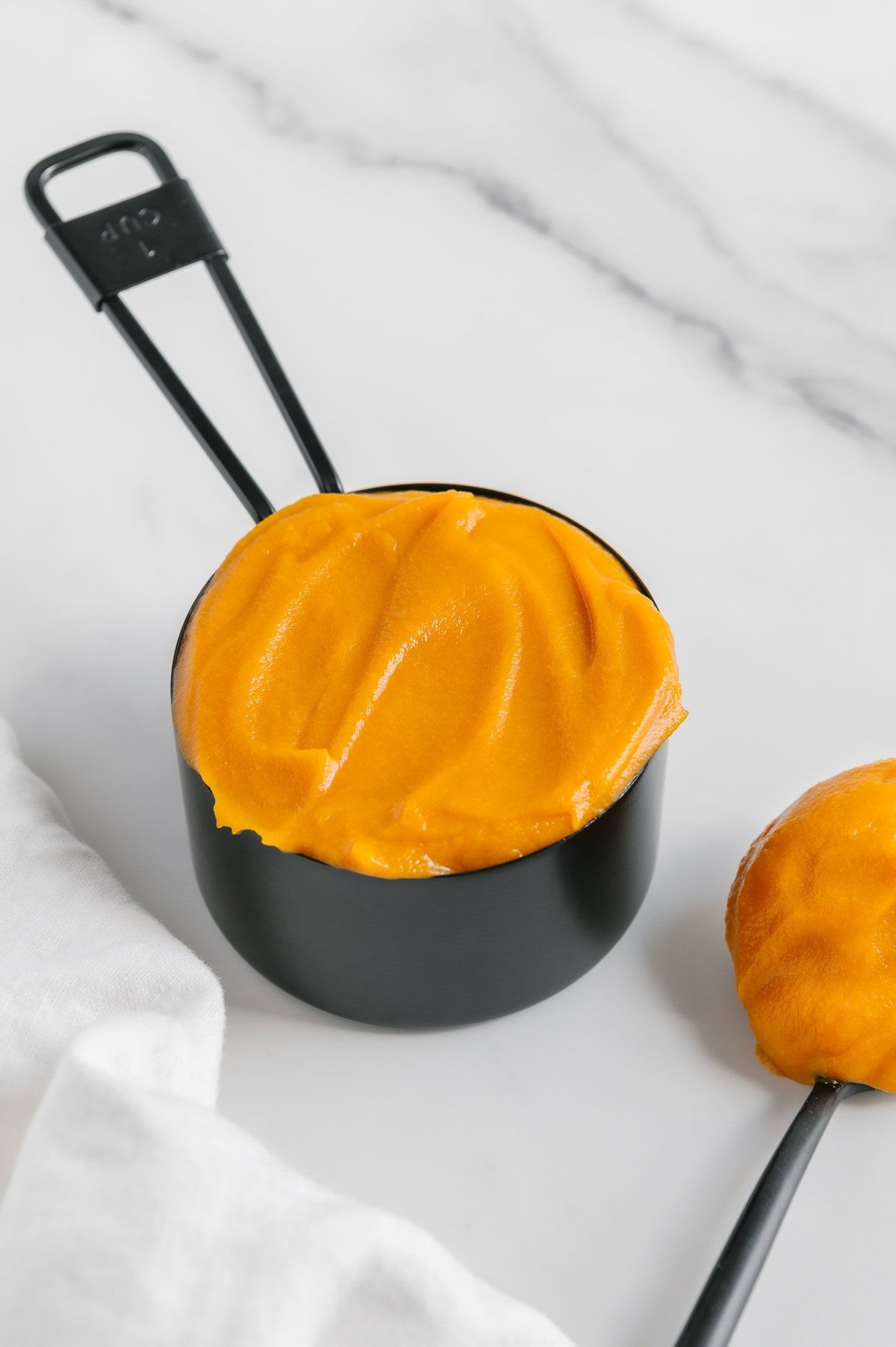Homemade sweet potato puree in a black measuring cup with a white marble background.