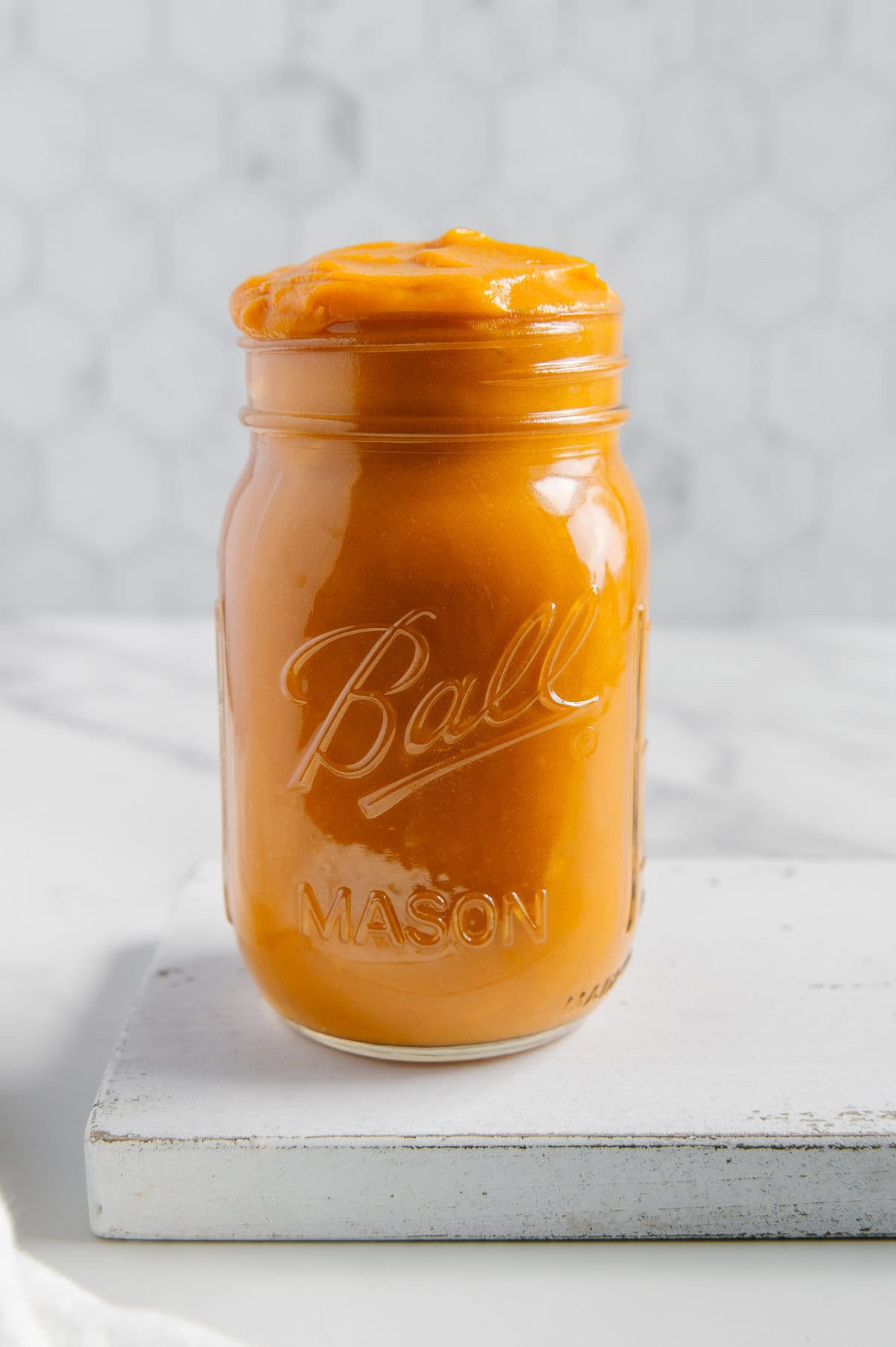 Homemade sweet potato puree in a glass mason jar with a white marble background.