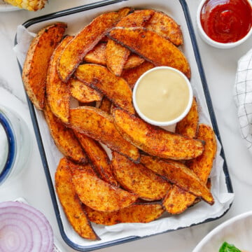 Crispy air fryer potato wedges on a white serving platter with served with honey mustard and ketchup.