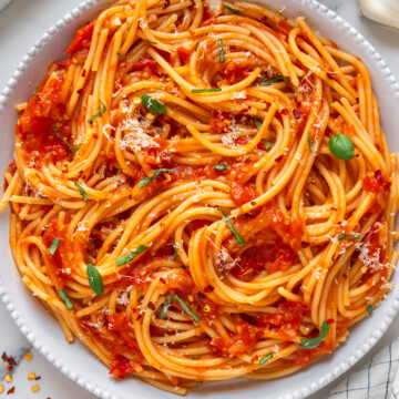 Spaghetti arrabbiata in a white bowl garnished with fresh basil with a white marble background.
