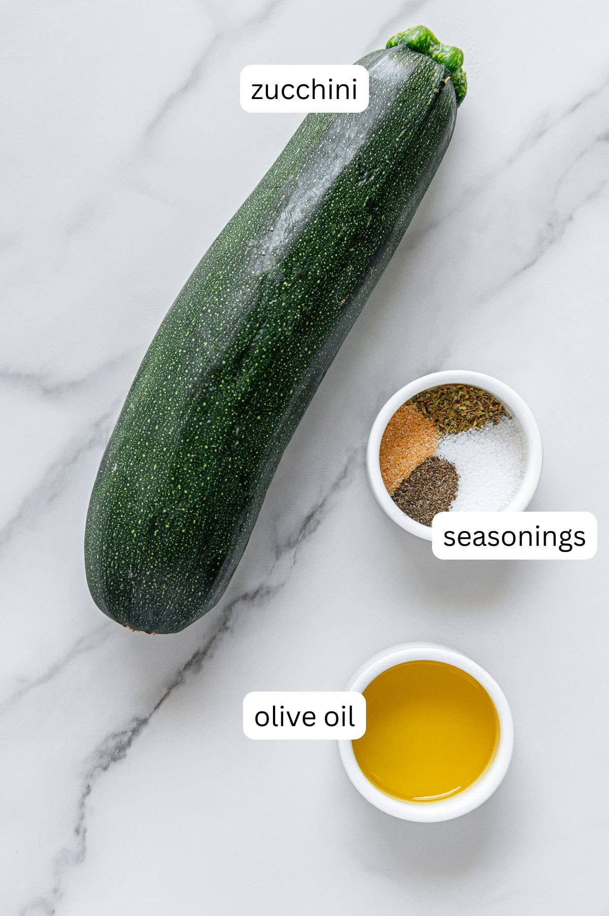 Zucchini, seasonings and olive oil on a white marble background.