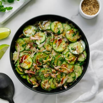 Sesame cucumber salad in a black bowl with a white marble background.
