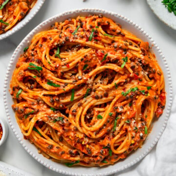 Black lentil marinara sauce served with spaghetti in a white bowl with a white marble background.