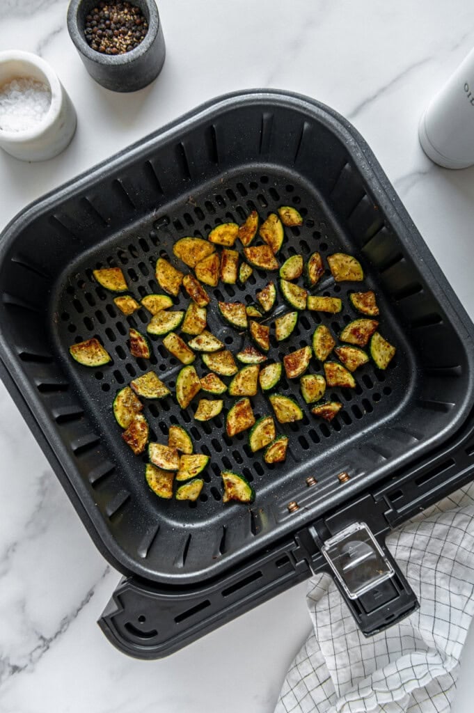 Air-fried zucchini in a black air fryer basket.