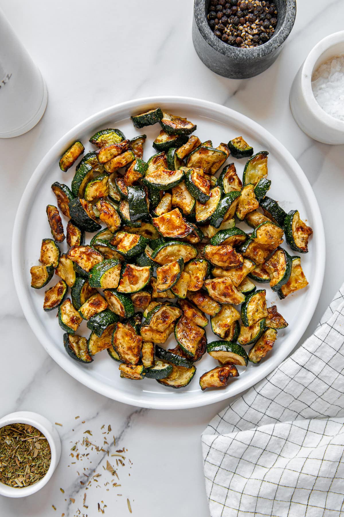 Golden brown zucchini pieces served on a white plate with a white marble background.