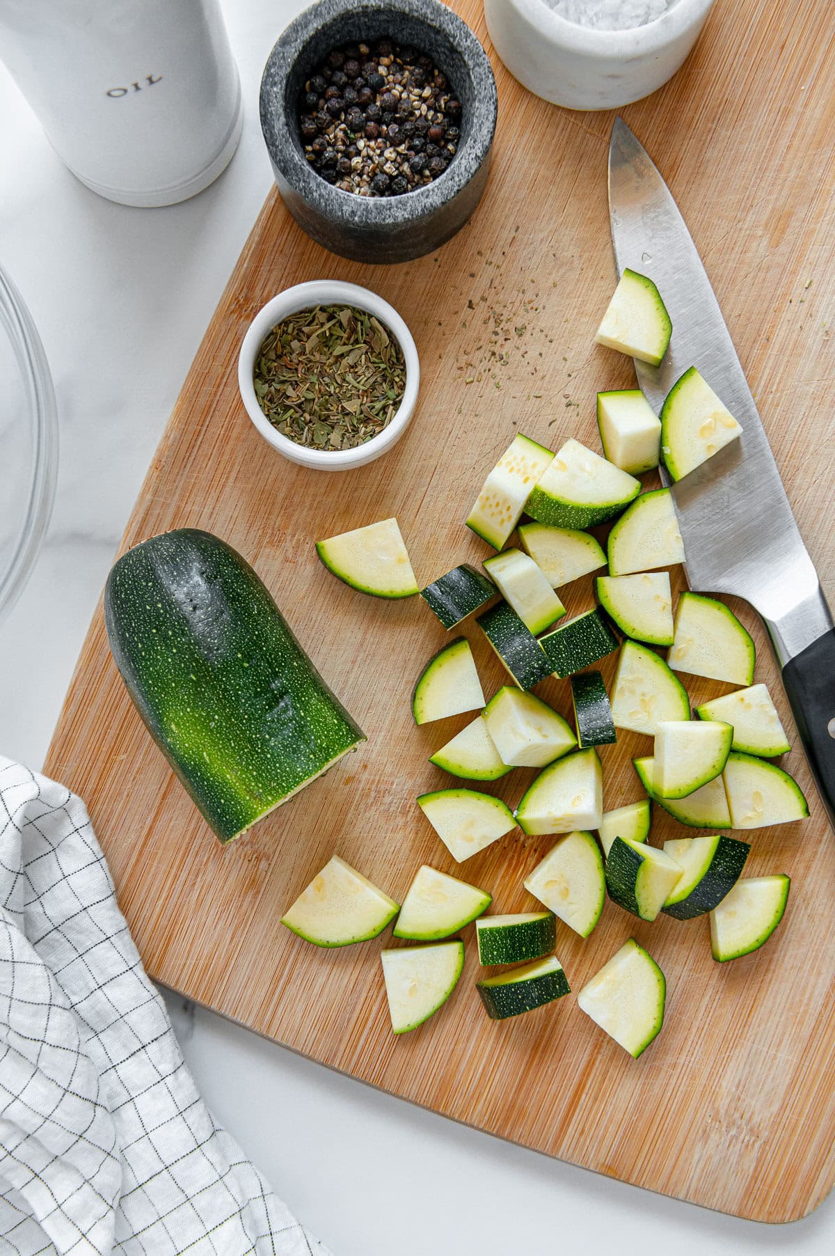 Diced zucchini on a wooden cutting board with a white marble background.