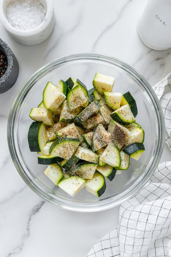 Diced zucchini with seasonings in a glass bowl.