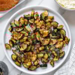 Air fryer zucchini sprinkled with parmesan cheese served on a round white plate with a white marble background.