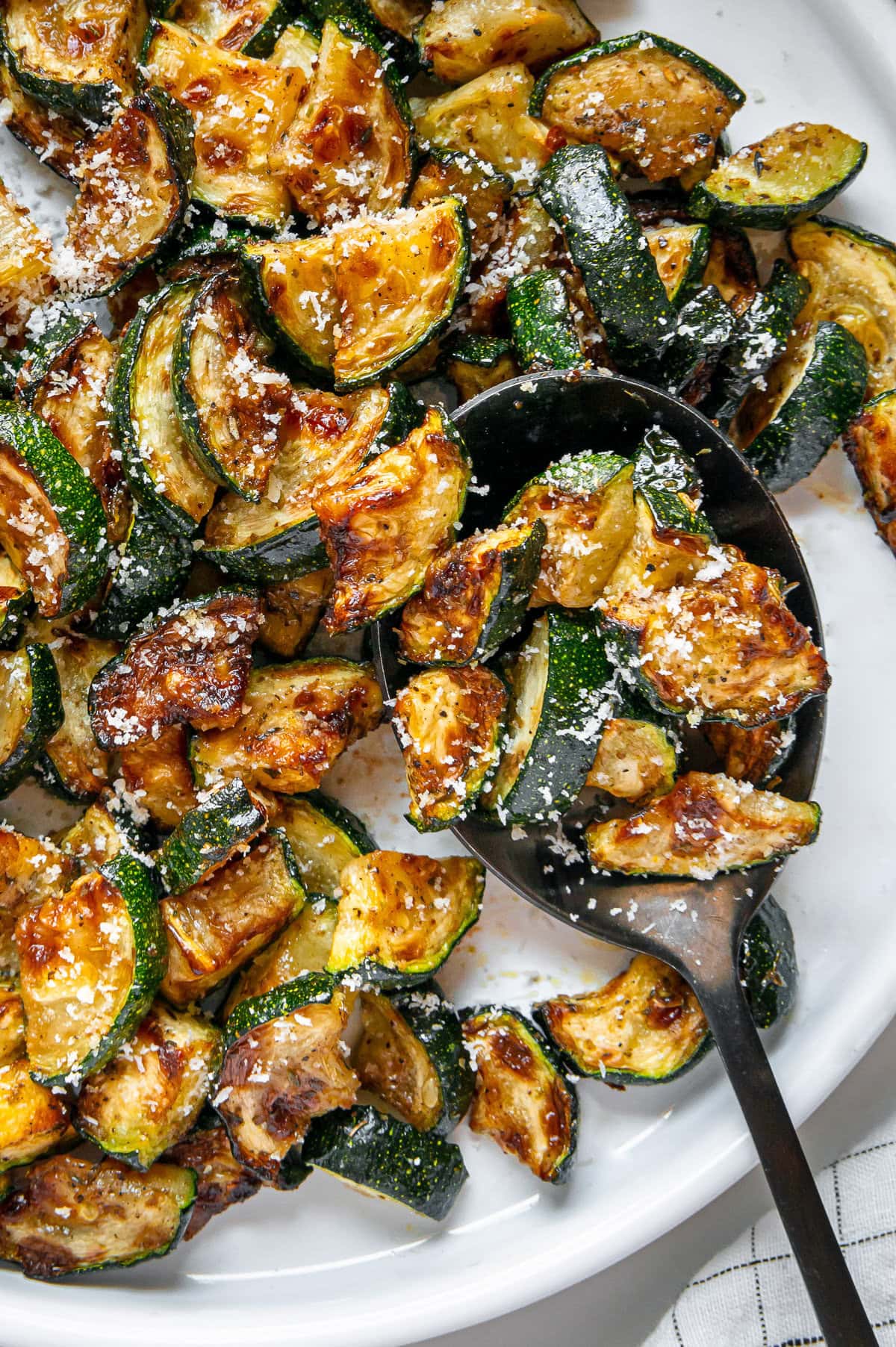 Crispy air fryer zucchini with parmesan cheese sprinkled overtop served with a black spoon.