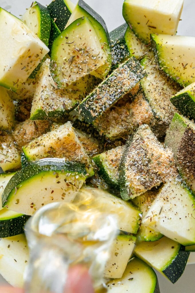 Diced seasoned zucchini with olive oil being poured overtop.
