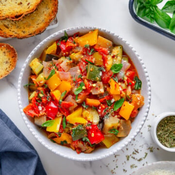 Ratatouille in a white bowl served with toasted bread with a white background.