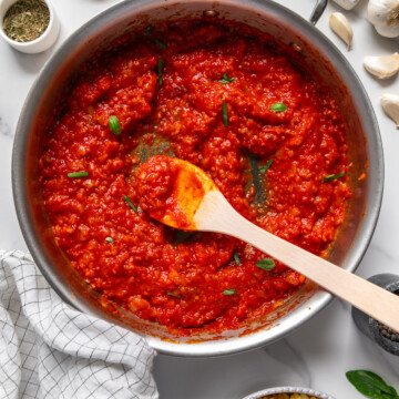 Homemade San Marzano tomato sauce in a saucepan with a white marble background.