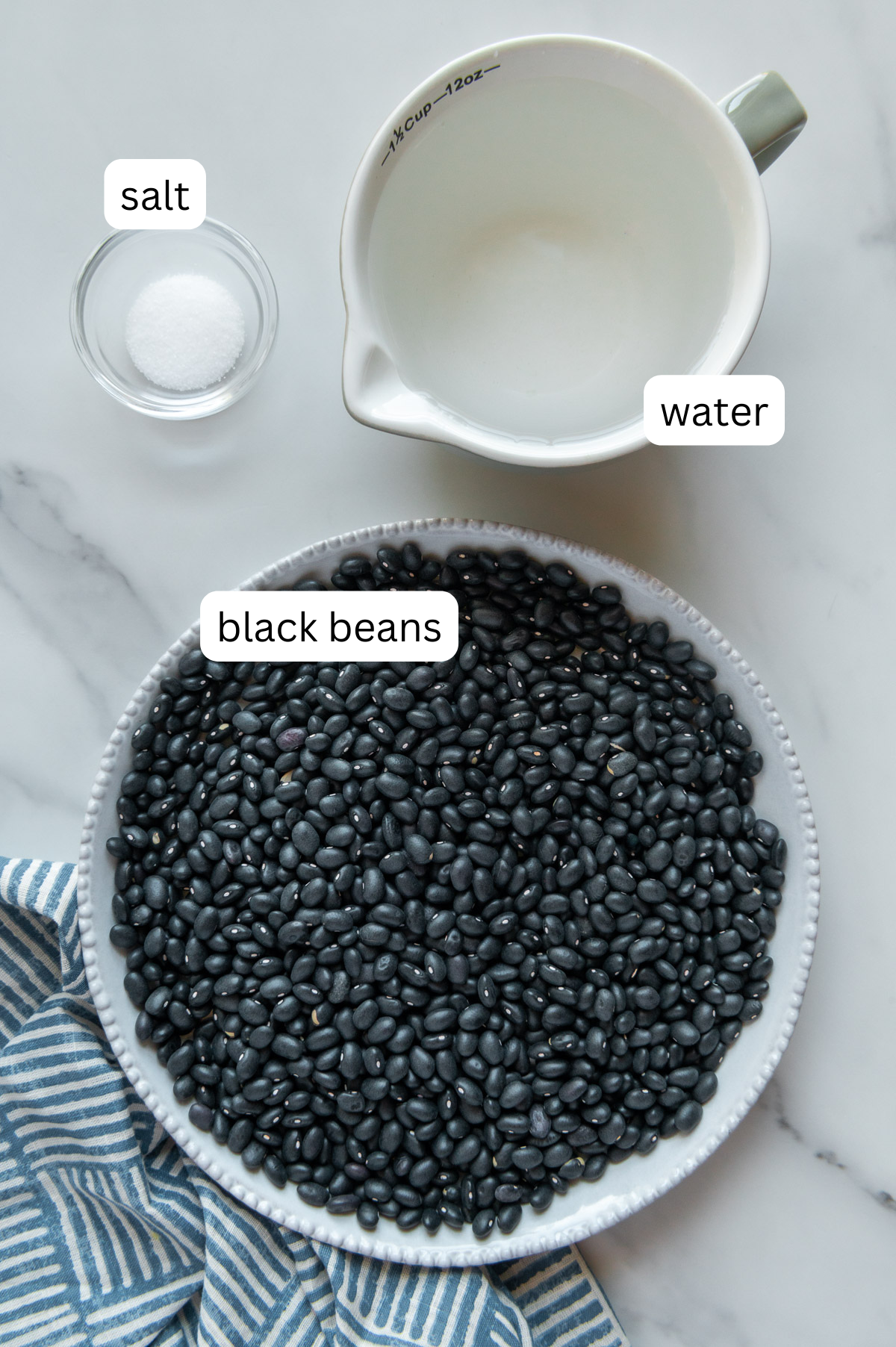 Dry black beans, water and salt with a white marble background.