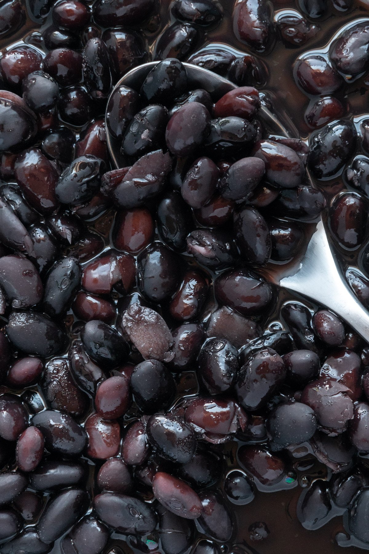 A spoon submerged in cooked black beans.