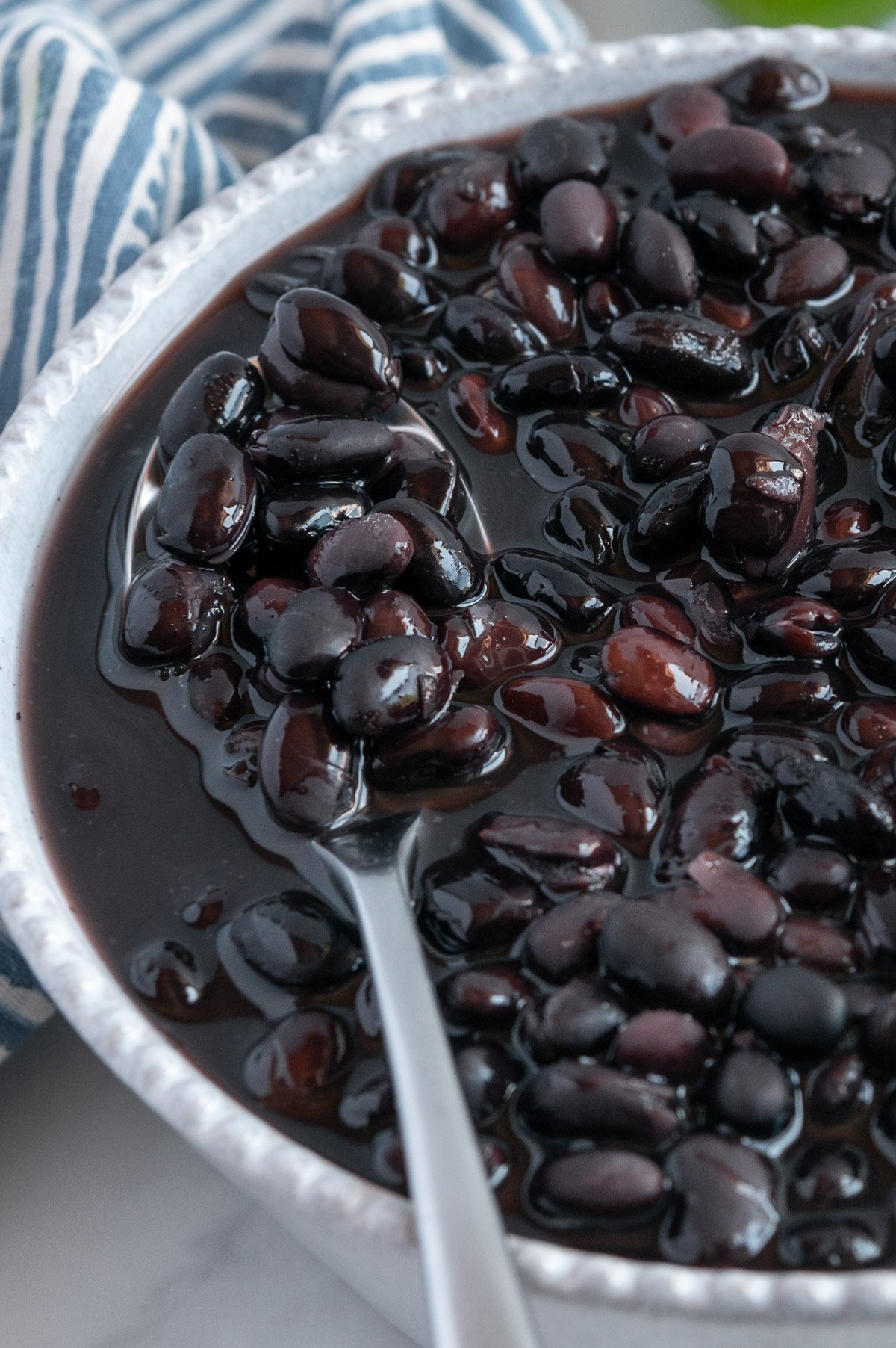 Cooked black beans in a white bowl served with a spoon.