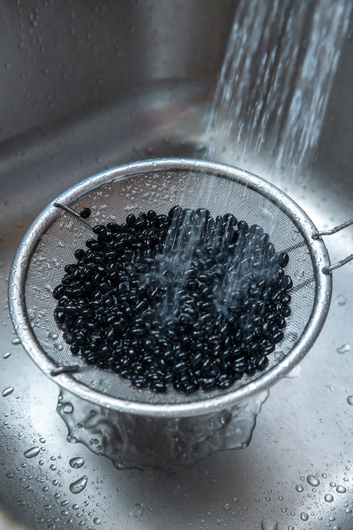 Rinsing dry black beans in a strainer in a sink.