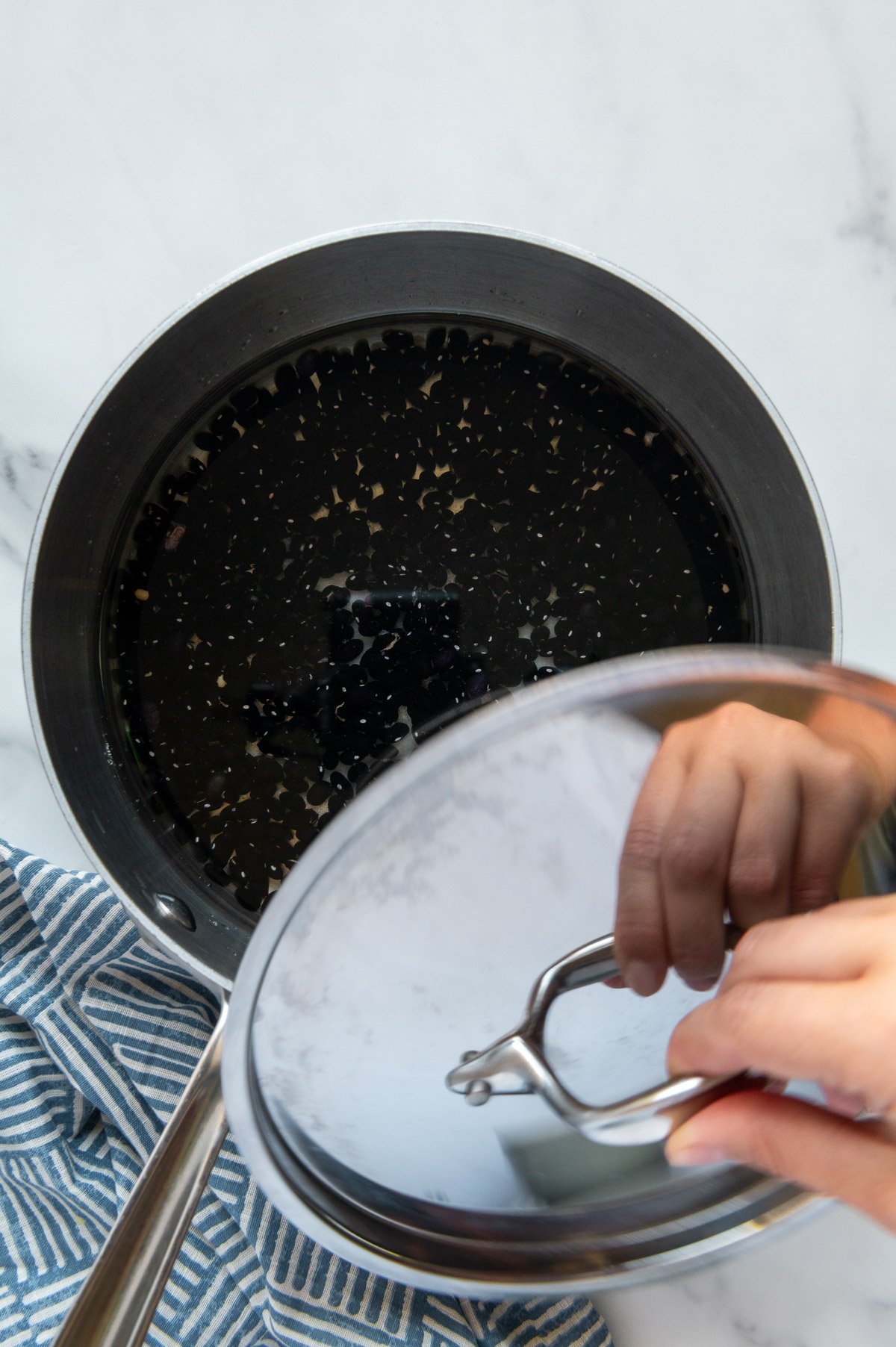 Covering black beans to cook in a pot with a white marble background.