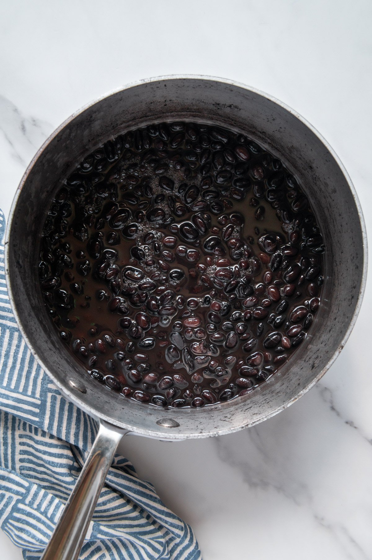 Cooked black beans in a pot with a white marble background.