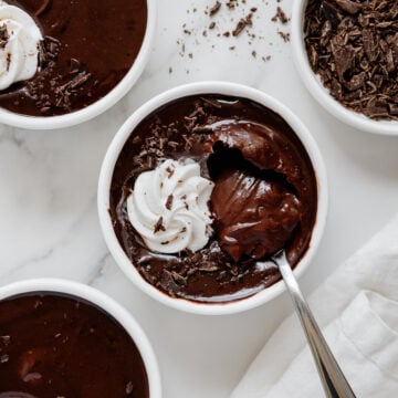 Vegan chocolate pudding topped with vegan whipped cream in white ramekins with a white marble background.