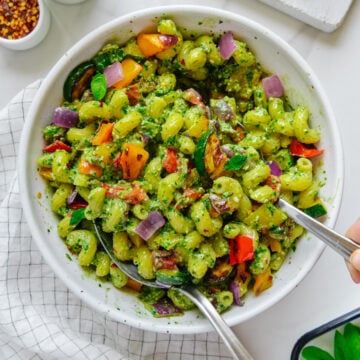 Pesto pasta with roasted veggies in a white bowl with a white marble background.