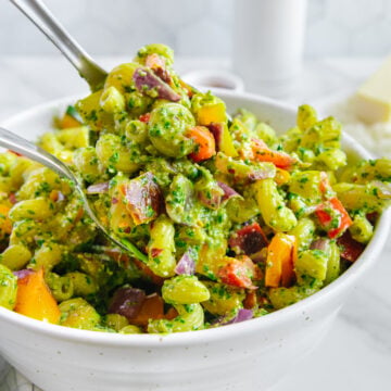 Pasta with pesto and roasted veggies in a white bowl with a white background.