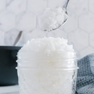 Homemade salt scrub in a small glass jar with a white background.