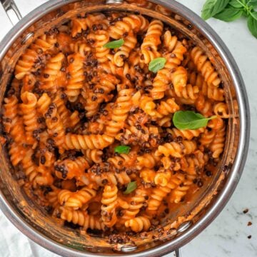 One-pot pasta garnished with fresh basil in a silver pot with a white marble background.