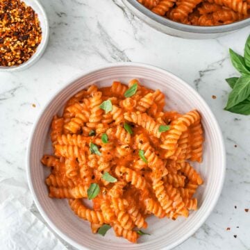 One-pot pasta garnished with fresh basil on a white plate with a white marble background.