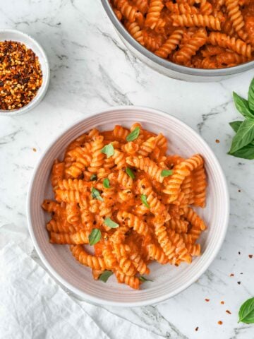 One-pot pasta garnished with fresh basil on a white plate with a white marble background.