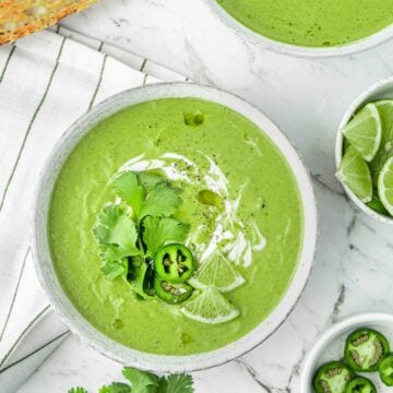 Vegan zucchini soup in two white bowls next to crusty bread with a white marble background.