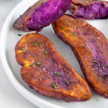 Roasted purple sweet potato halves arranged on a white plate with a white background.