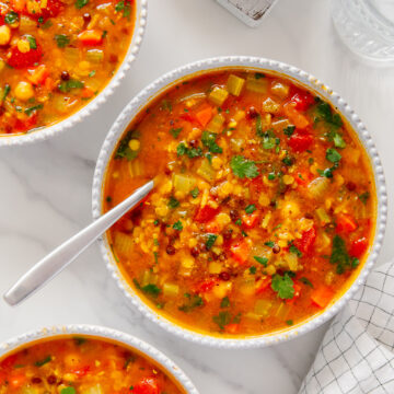 Moroccan harira soup served in white bowls next to crusty bread with a white marble background.
